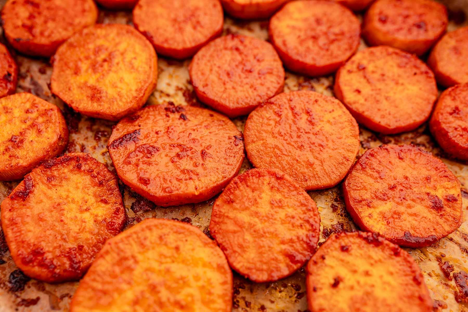 A close-up reveals the savory beauty of baked sweet potato slices, perfectly roasted on a baking sheet.