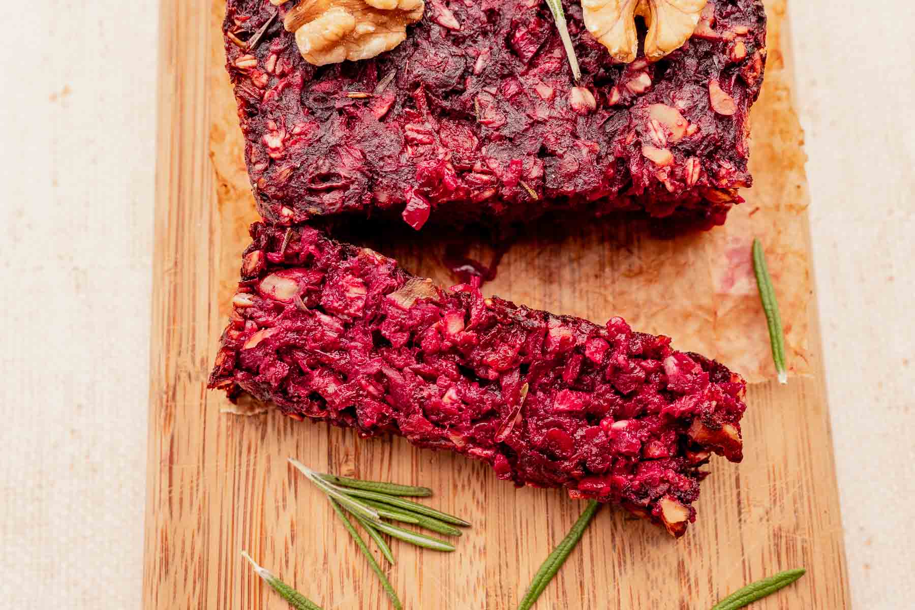 A sliced loaf of beetroot and nut bread on a wooden board, garnished with rosemary and walnuts, complements a hearty vegetarian roast perfectly.
