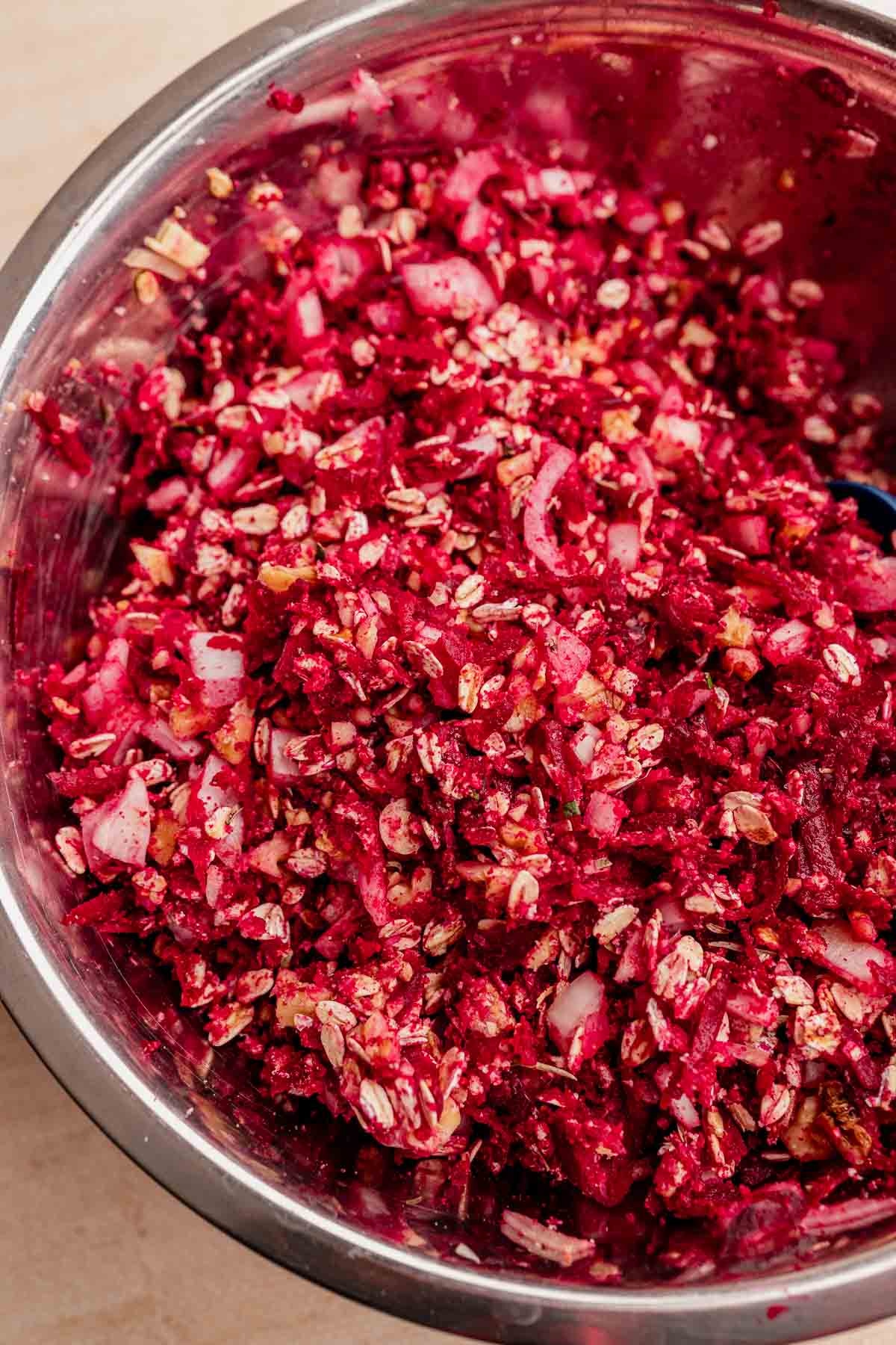 Close-up of a metal bowl filled with a colorful mixture of finely chopped beets, oats, and onions, creating the perfect base for a delicious vegetarian roast.