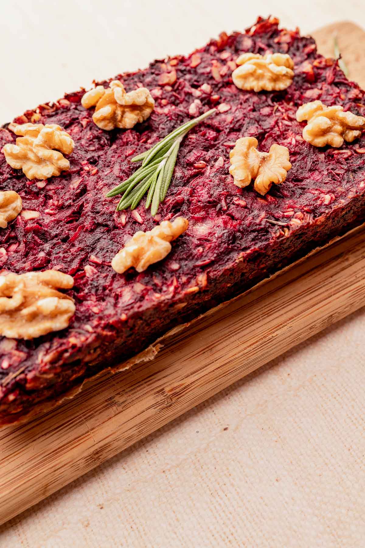 Rectangular beet and walnut loaf serves as a delightful vegetarian roast, featuring walnut halves and a sprig of rosemary on top, all elegantly placed on a wooden board.