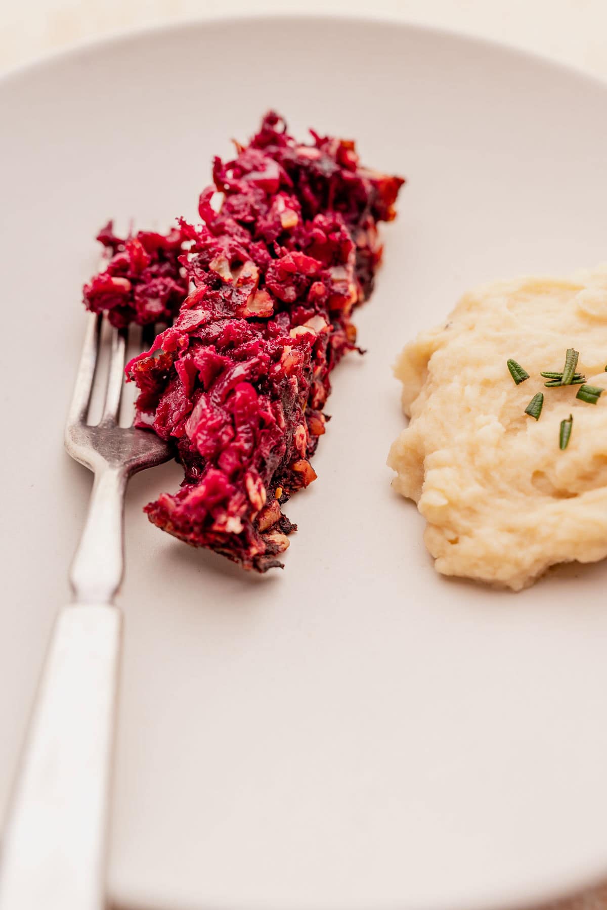 A fork rests on a plate, accompanied by a beet salad on one side and mashed potatoes garnished with chives on the other, complementing a delightful vegetarian roast.