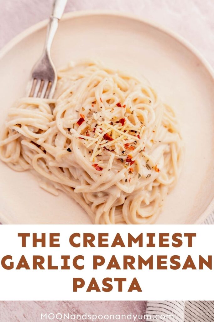 A plate of creamy garlic parmesan pasta with a fork, topped with shredded cheese and red pepper flakes.