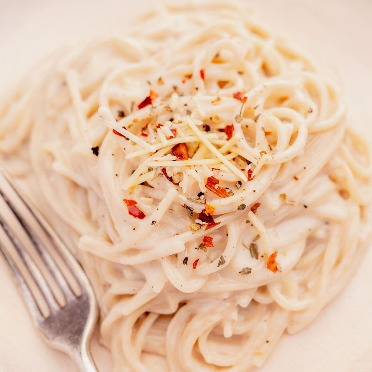 A plate of creamy pasta topped with grated cheese and red pepper flakes, with a fork placed nearby.