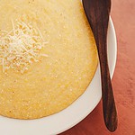 A plate of creamy yellow polenta topped with grated cheese, served with a wooden spoon on a white plate.