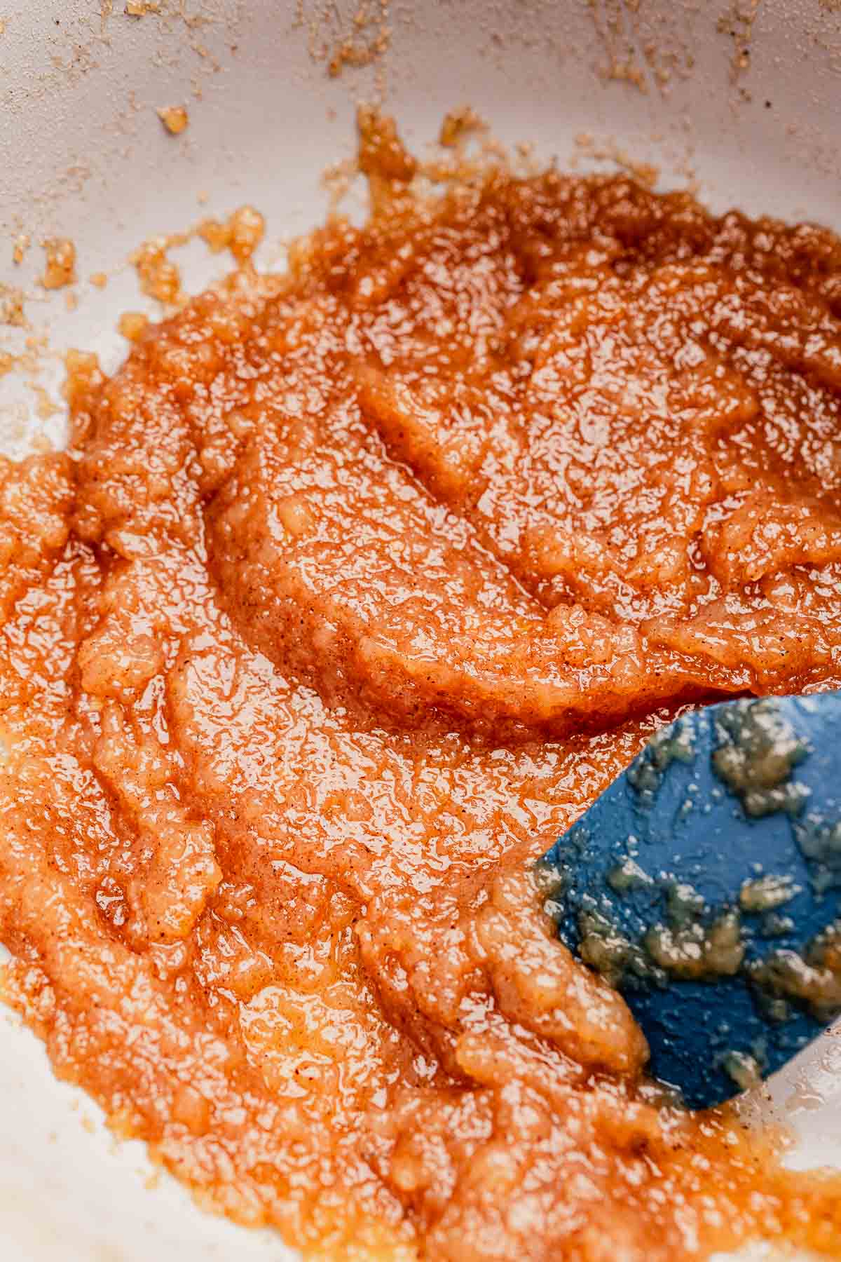 Close-up of a pot containing a thick, brown, textured mixture being stirred with a blue spatula.