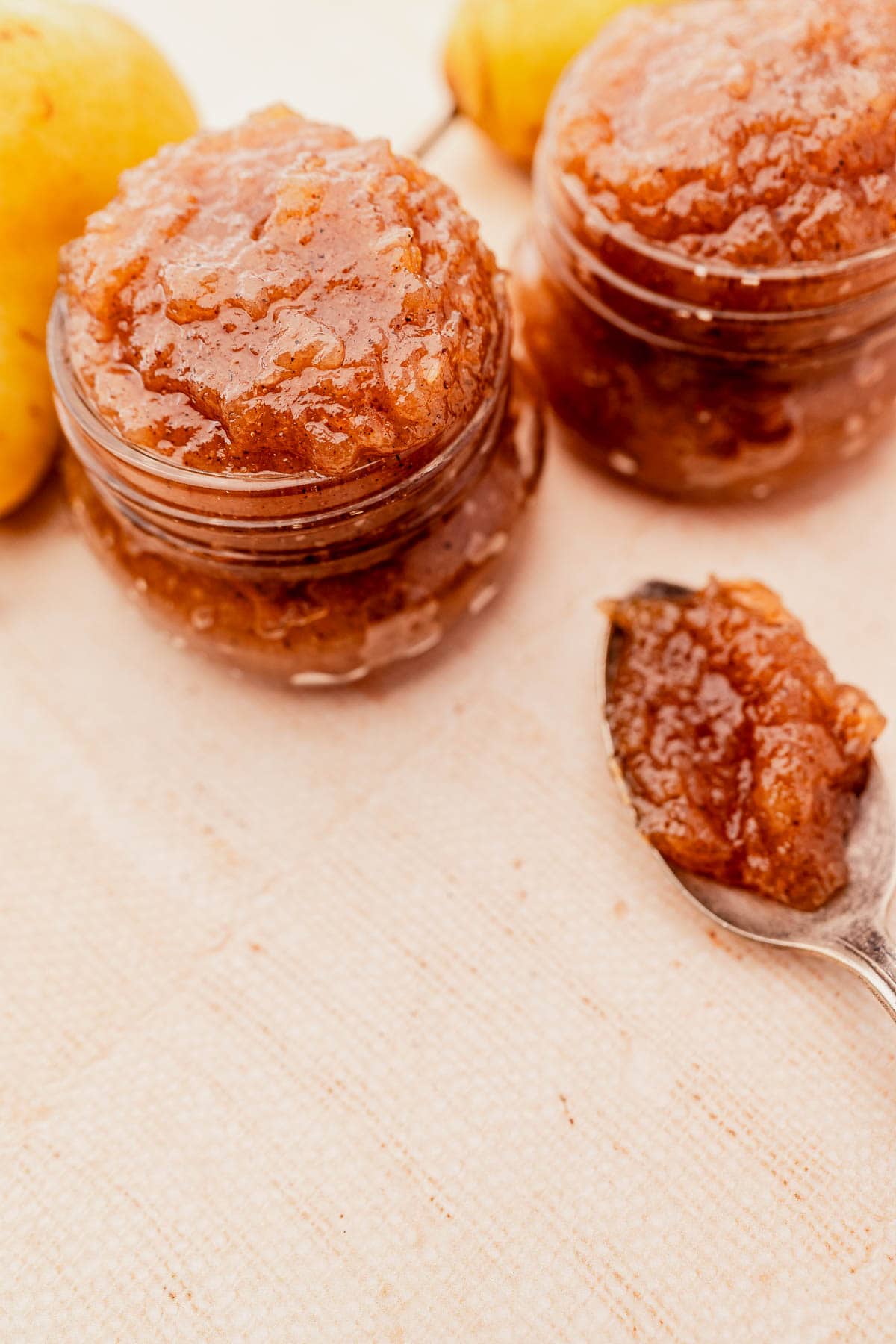Two jars of pear preserves on a cloth with a spoonful beside them and whole pears in the background.