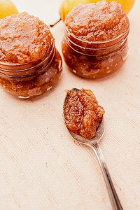 Two jars of pear preserves next to a spoonful of the preserve on a light cloth background.