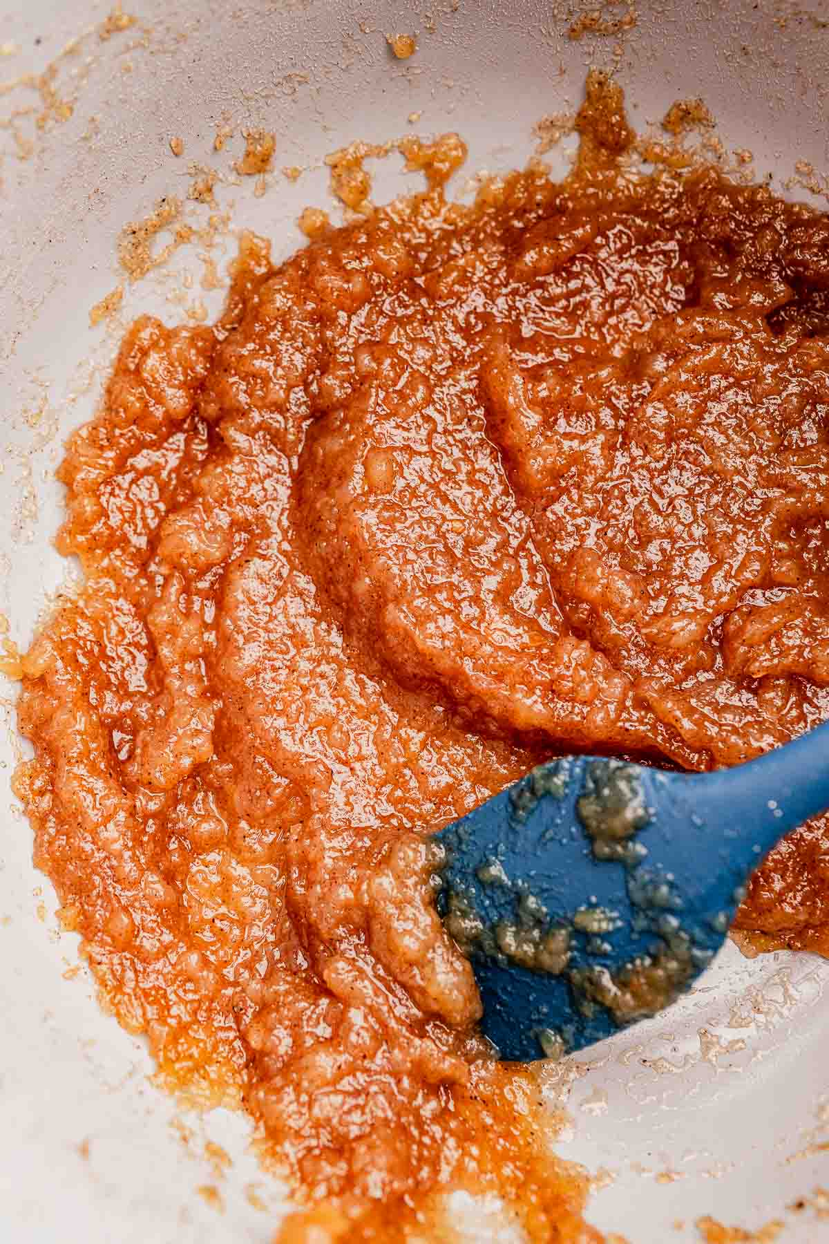 Close-up of a brown, chunky mixture being stirred with a blue spatula in a white bowl.