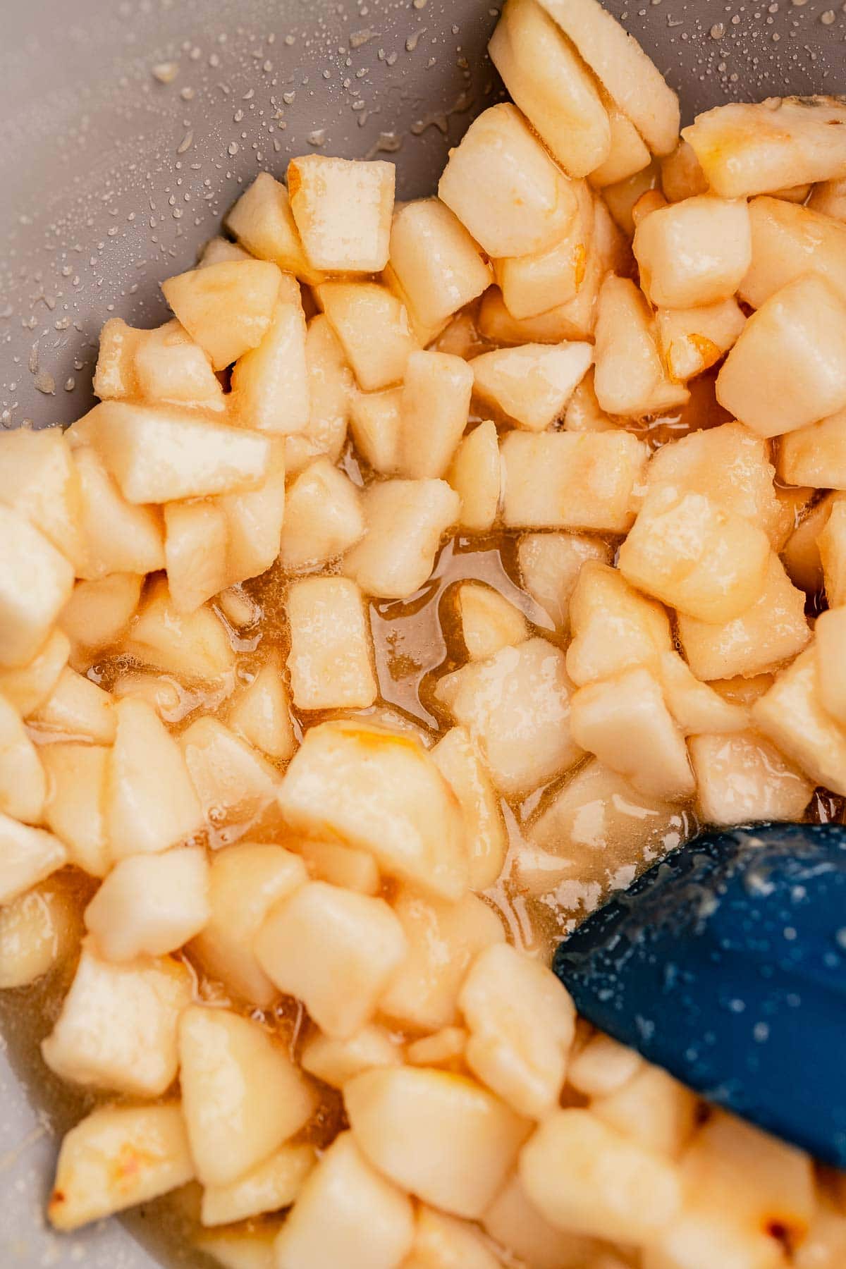 Diced apples in a bowl with a blue spatula, covered in liquid.
