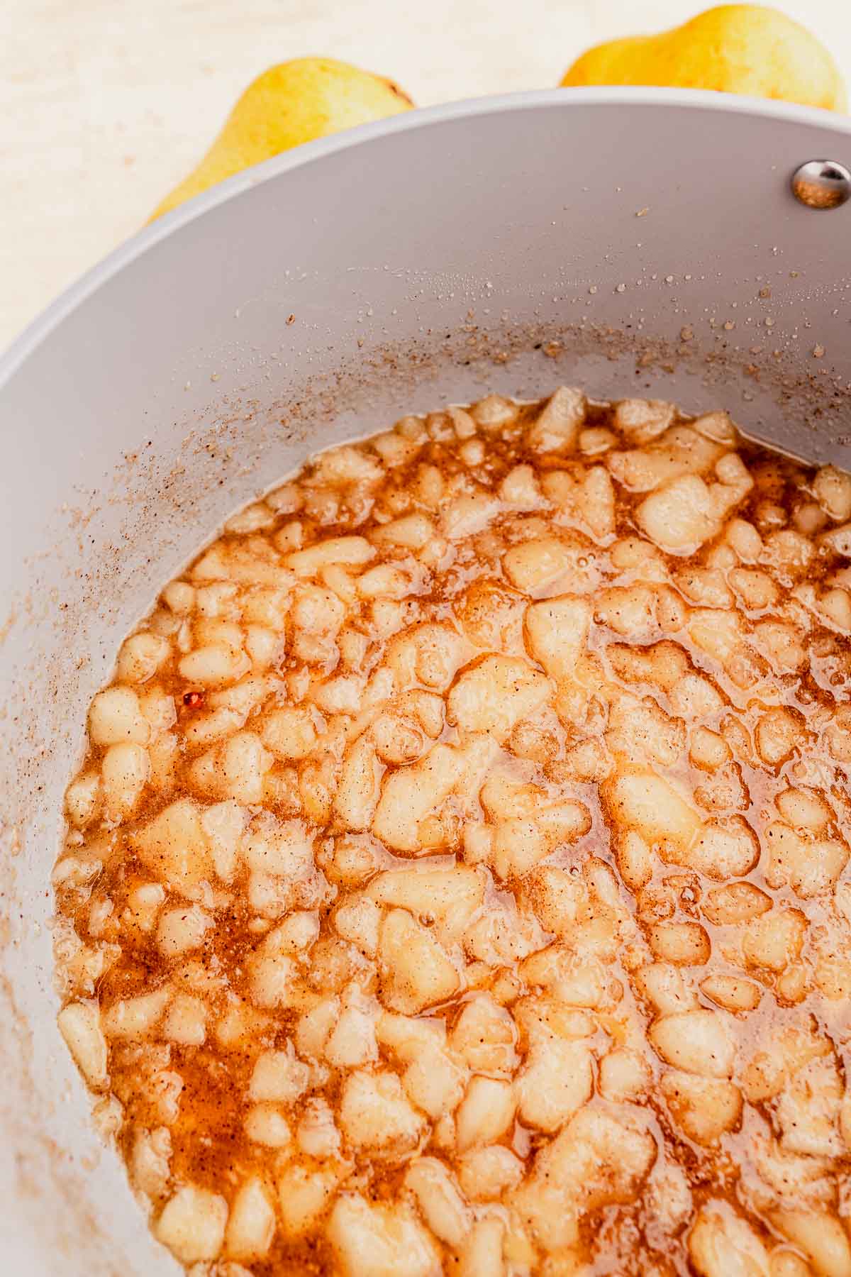 A pot filled with simmering applesauce and visible chunks, with pears partially visible in the background.