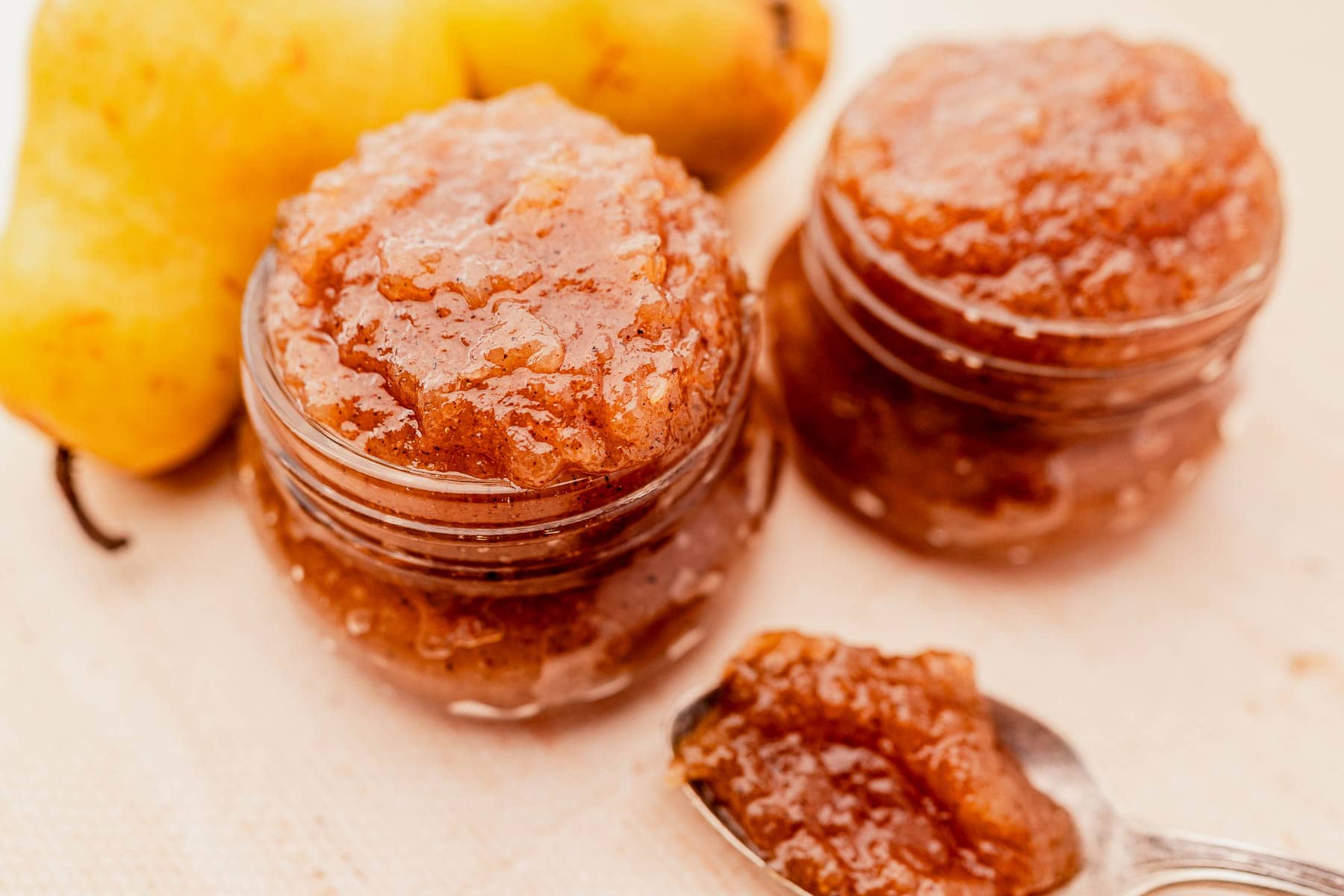 Jars of pear jam with a spoon, and whole pears in the background.