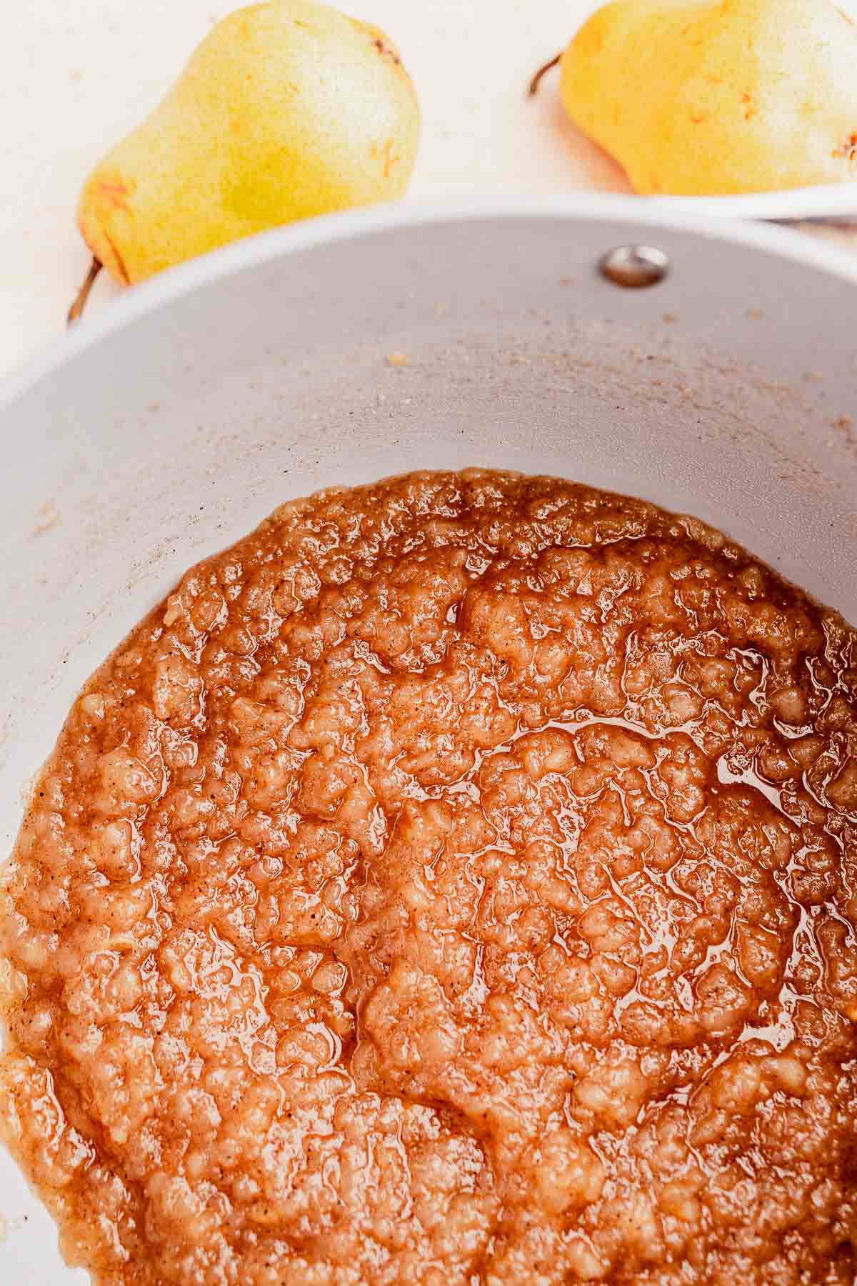 Close-up of pear sauce in a cooking pot with two whole pears in the background.