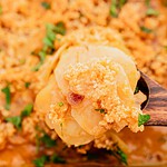Close-up of a wooden spoon lifting a serving of scalloped potatoes with golden breadcrumbs and parsley garnish.