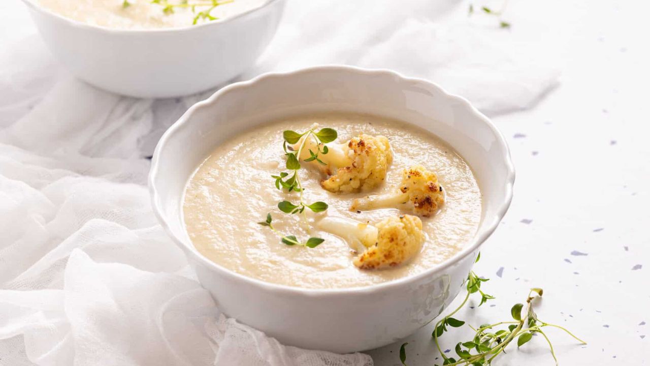 An image of roasted cauliflower soup in a white bowl, with fresh thyme on the side.