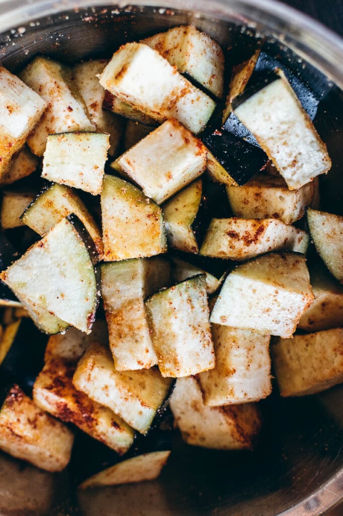 Diced eggplant pieces, perfectly seasoned with spices, are ready to be crisped to perfection in an air fryer, all nestled in a metal bowl.