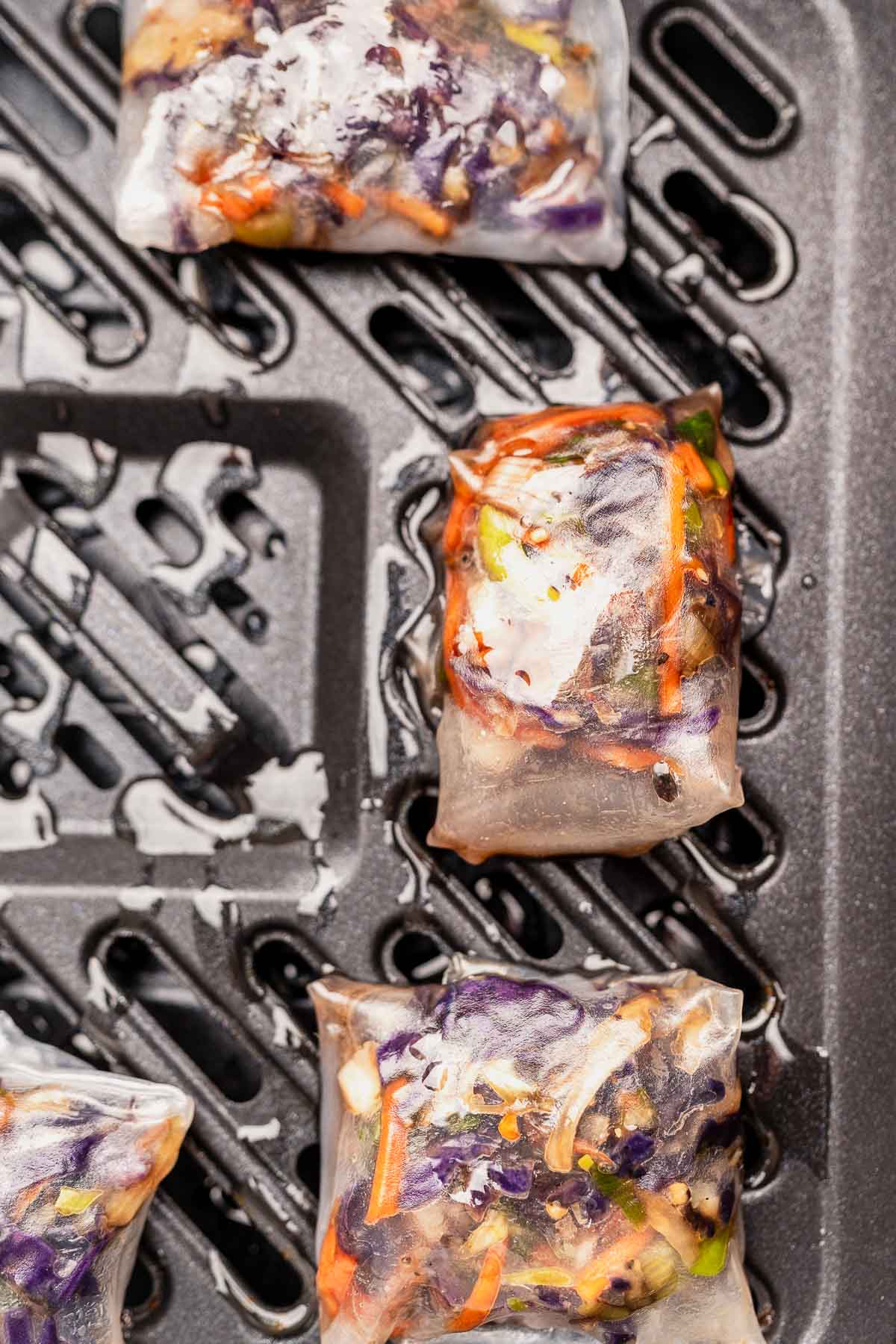 Four vegetable-filled rice paper rolls sizzling on a grill pan, reminiscent of the crispy delight you might achieve with air fryer rice paper dumplings.