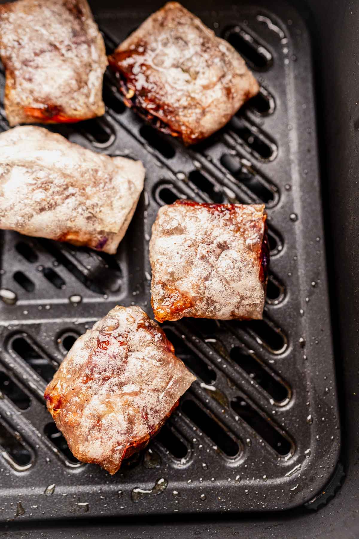 Five powdered sugar-dusted pastry squares rest elegantly in an air fryer basket, reminiscent of delicate rice paper dumplings.