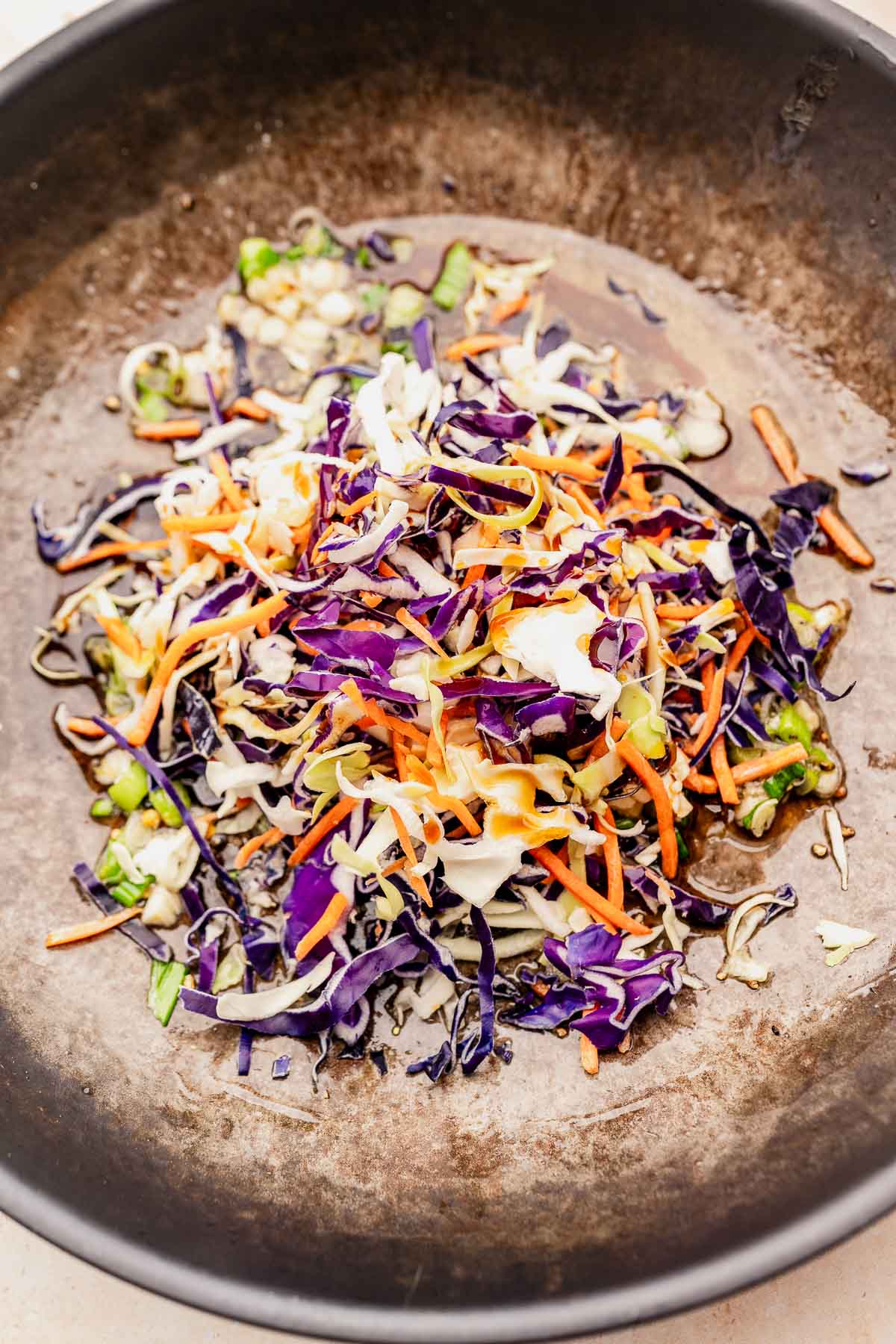 Chopped vegetables, including purple cabbage, carrots, and green onions, sizzle in a dark pan beside perfectly crisp air-fried rice paper dumplings.