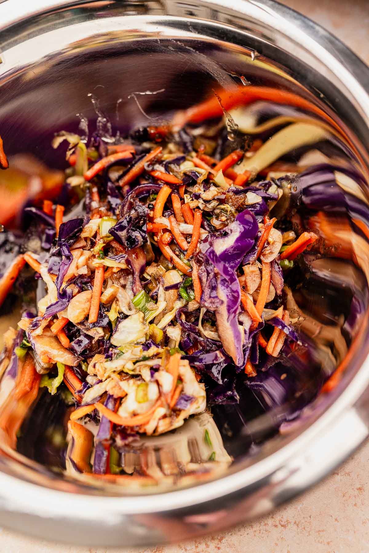 Close-up of a stainless steel bowl containing a colorful coleslaw mixture with shredded carrots, purple cabbage, and green vegetables, perfect for pairing with air fryer rice paper dumplings.