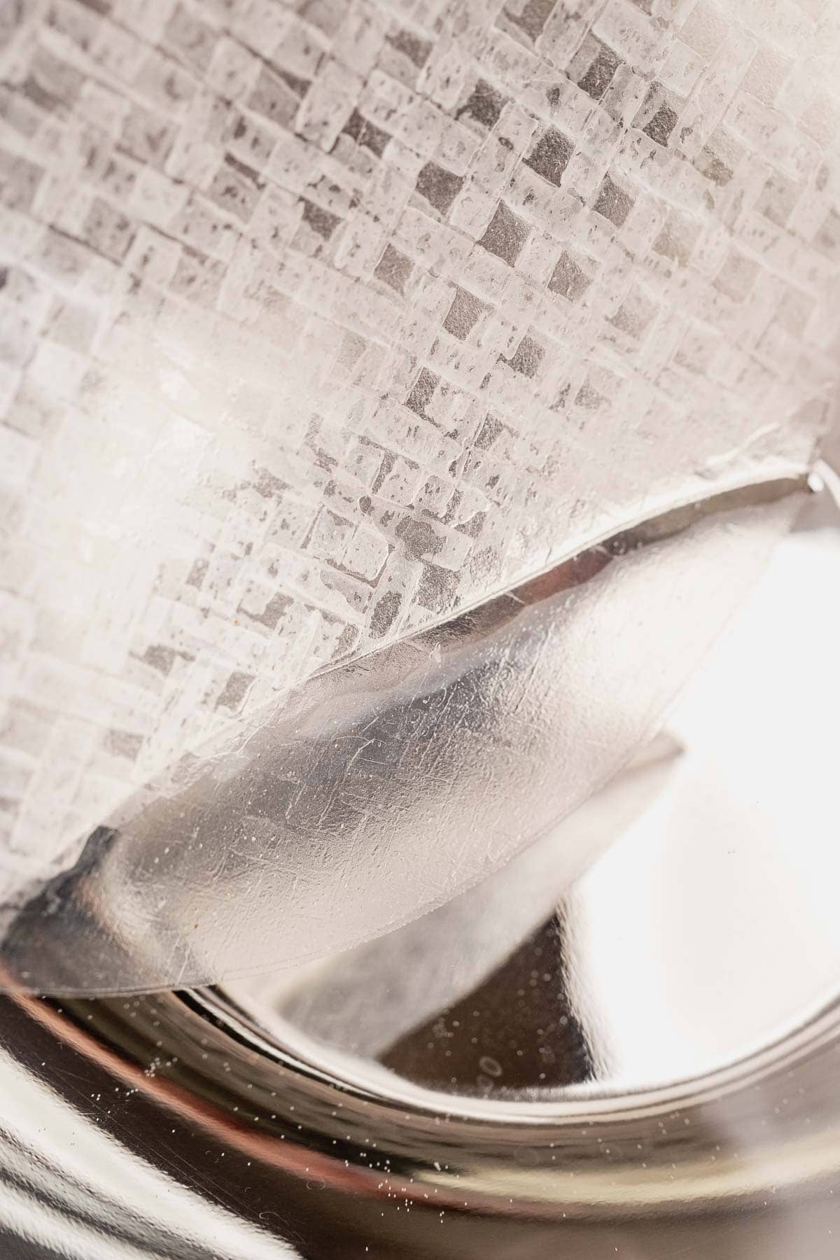 Close-up of translucent textured rice paper partially covering a shiny, metallic spoon, reminiscent of the delicate wrapping used in air fryer dumplings.