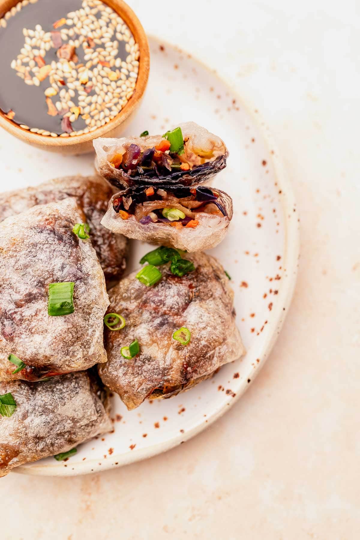 Plate of crispy rice paper spring rolls filled with colorful vegetables, garnished with green onions, alongside a small bowl of soy sauce with sesame seeds. These delightful bites can also be prepared as air fryer dumplings for a healthier twist.