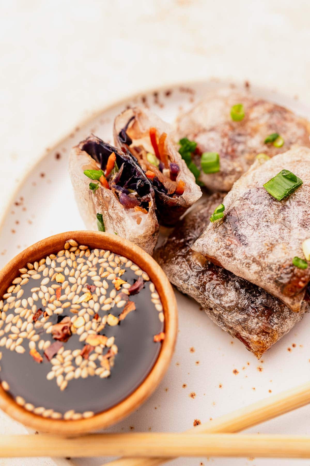 Plated air fryer rice paper dumplings filled with sliced vegetables, accompanied by a bowl of soy sauce adorned with sesame seeds. Chopsticks are placed nearby, ready to enhance the experience.