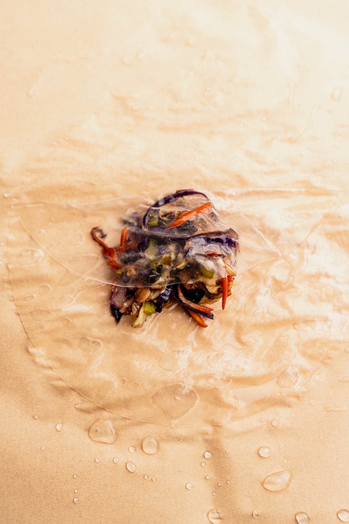 A vegetable mixture rests on a circular rice paper sheet, ready to become delicious air fryer rice paper dumplings, with glistening water droplets scattered on the beige surface.