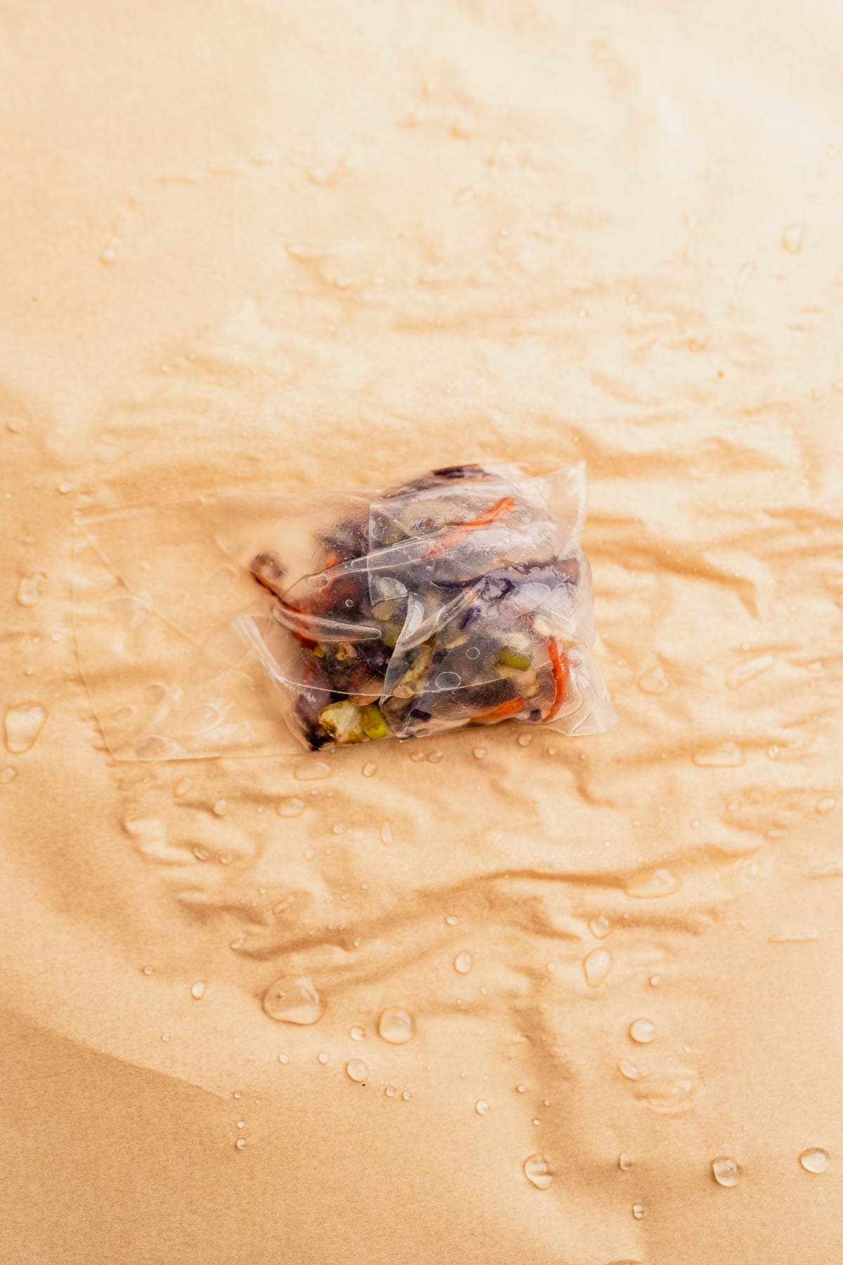 A vacuum-sealed package of mixed vegetables and herbs rests on a wet brown paper surface, perfectly prepped for crafting delicious rice paper dumplings or a quick air fryer meal.