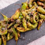 A pile of roasted green peppers sprinkled with coarse salt on a dark slate surface.