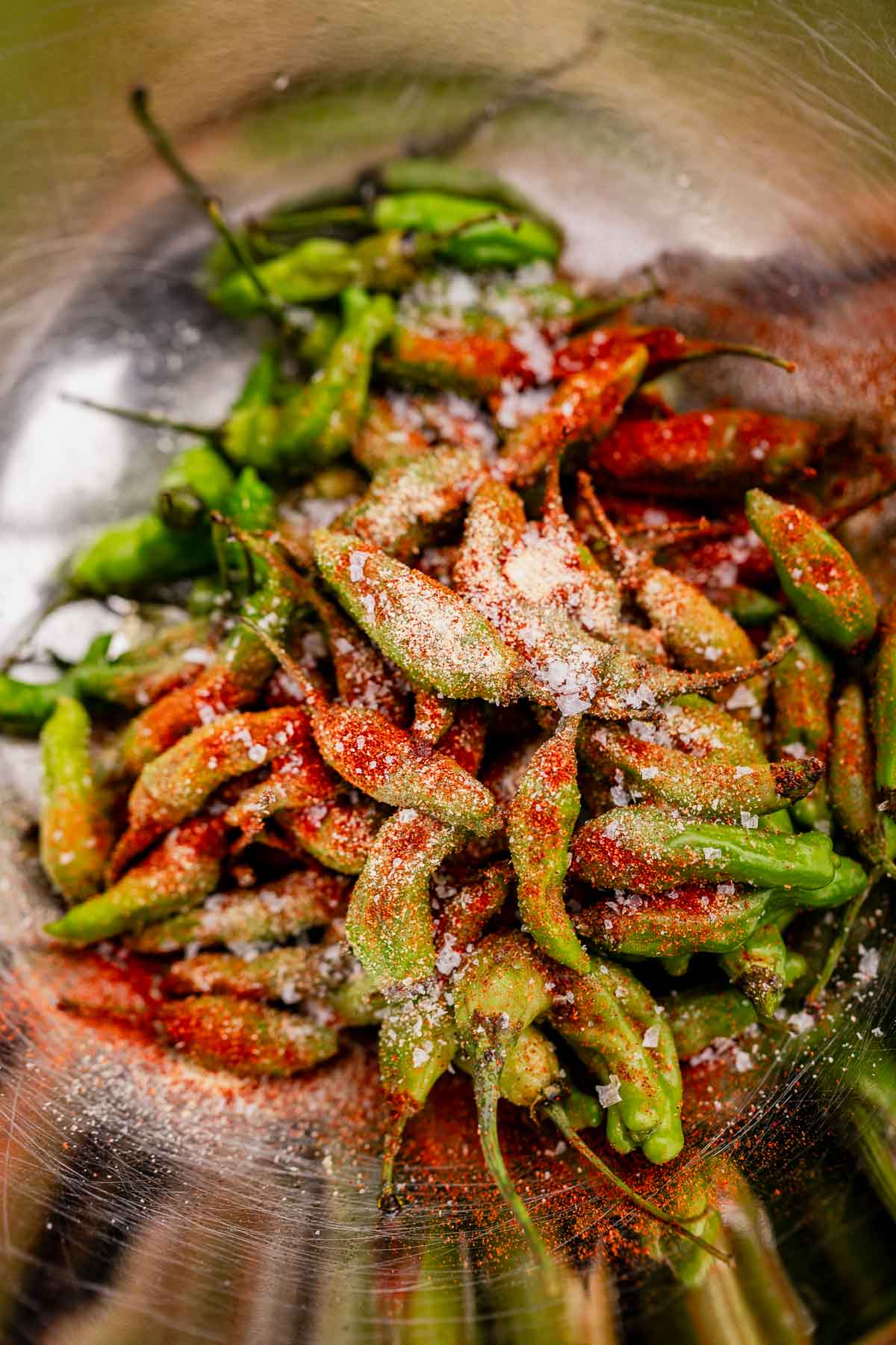 A bowl of vibrant green and red chili peppers, reminiscent of air fryer shishito peppers, sprinkled with coarse salt.