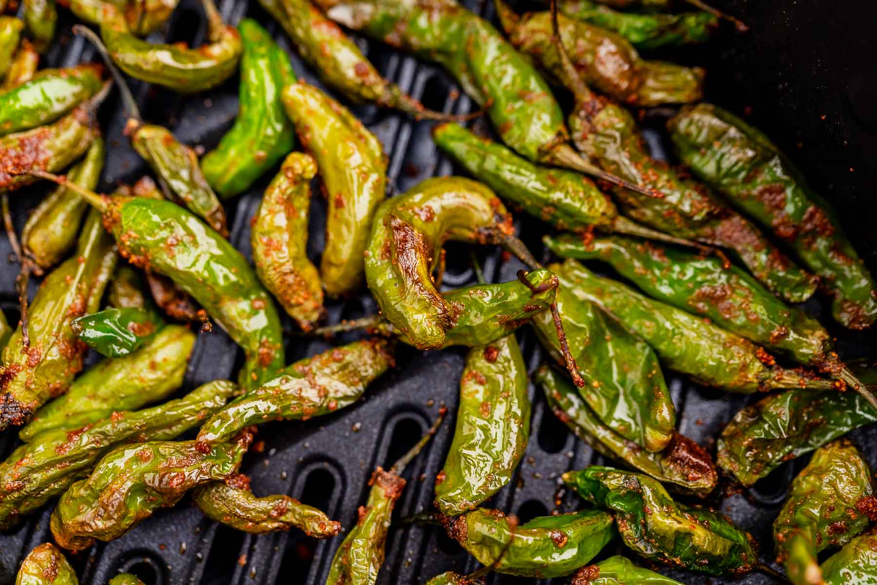 Close-up of roasted shishito peppers on a grill, their glossy surface and char marks evoking the enticing crispness of air fryer shishito peppers.