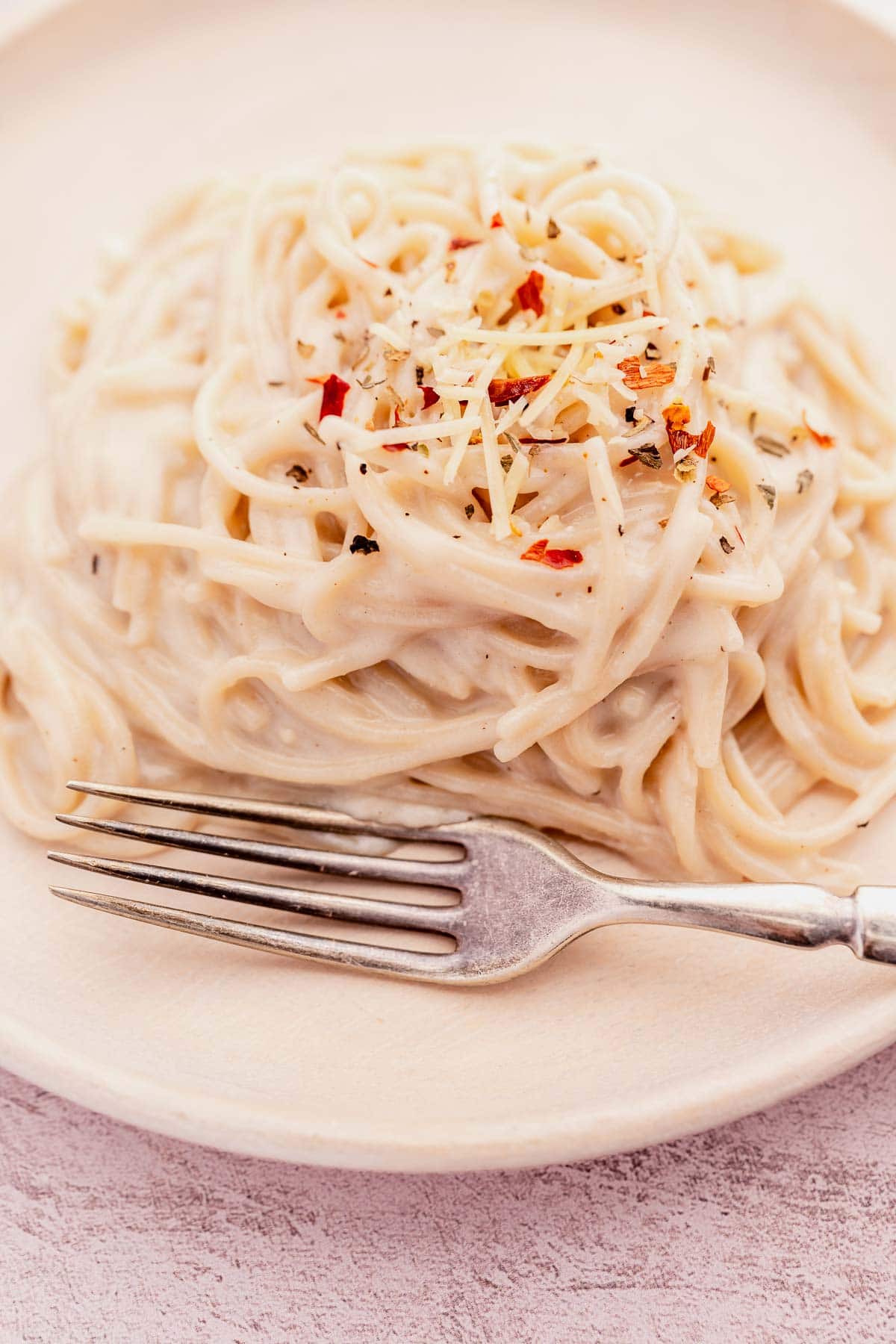 Plate of creamy garlic parmesan pasta topped with grated cheese and herbs, with a fork placed beside it.