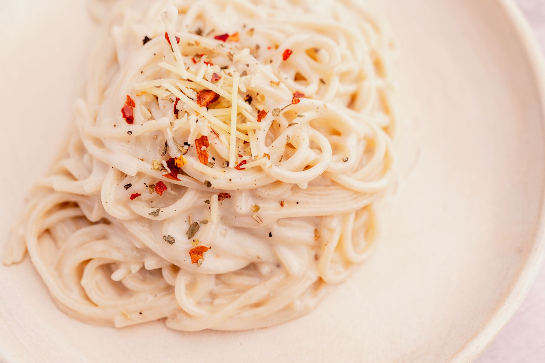 A plate of garlic parmesan spaghetti topped with grated cheese and red pepper flakes sits elegantly on a light-colored dish.
