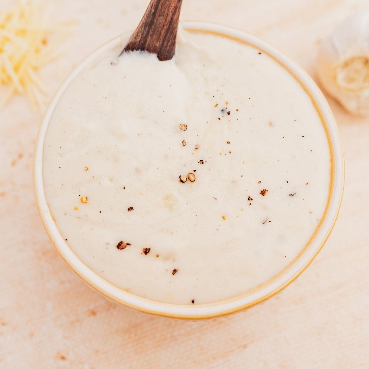A bowl of creamy sauce topped with cracked black pepper, with a wooden spoon resting in it.