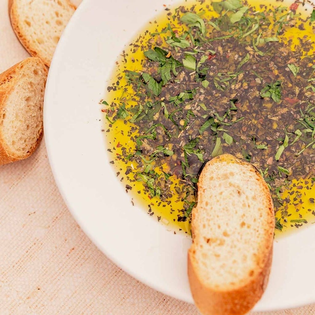 A white plate with olive oil, herbs, and two slices of bread.