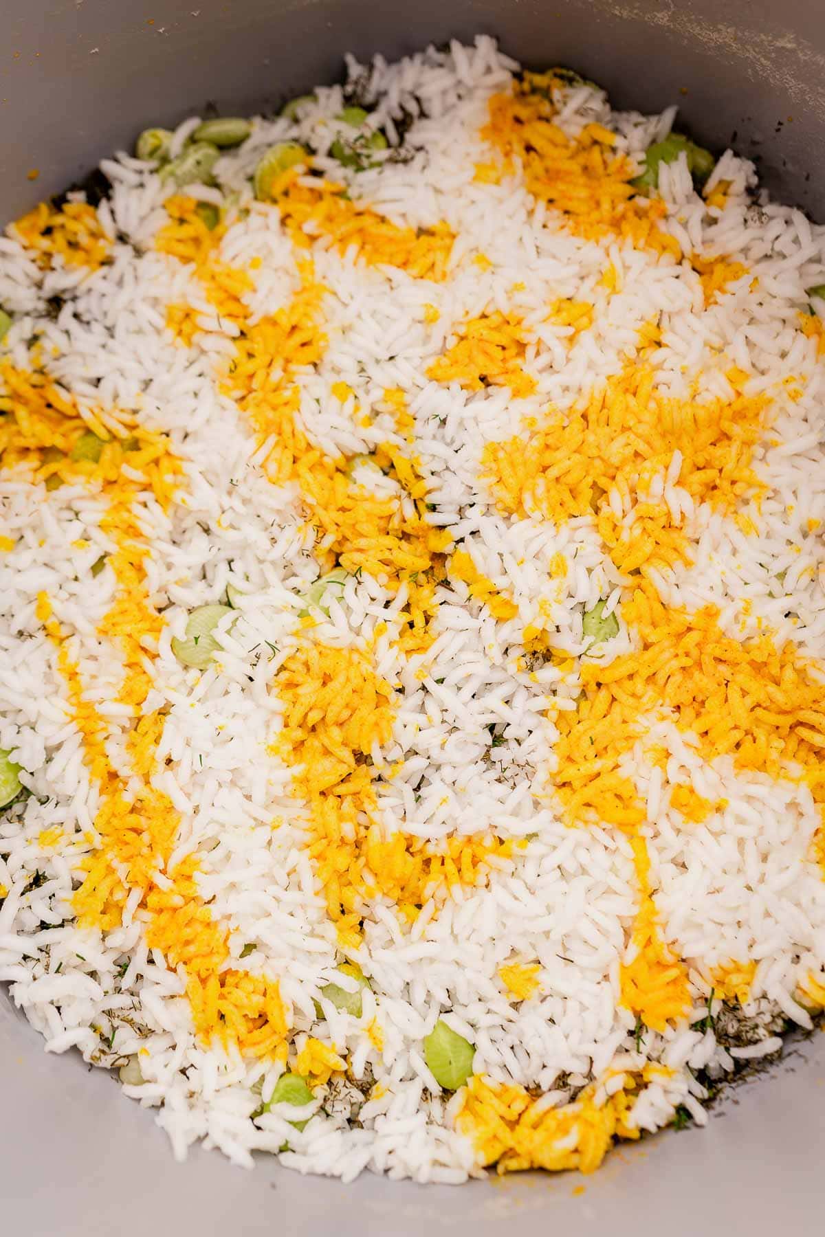 Close-up of dill rice with vibrant yellow strands of saffron on top, mingling harmoniously with fresh green herbs in a pan or pot.