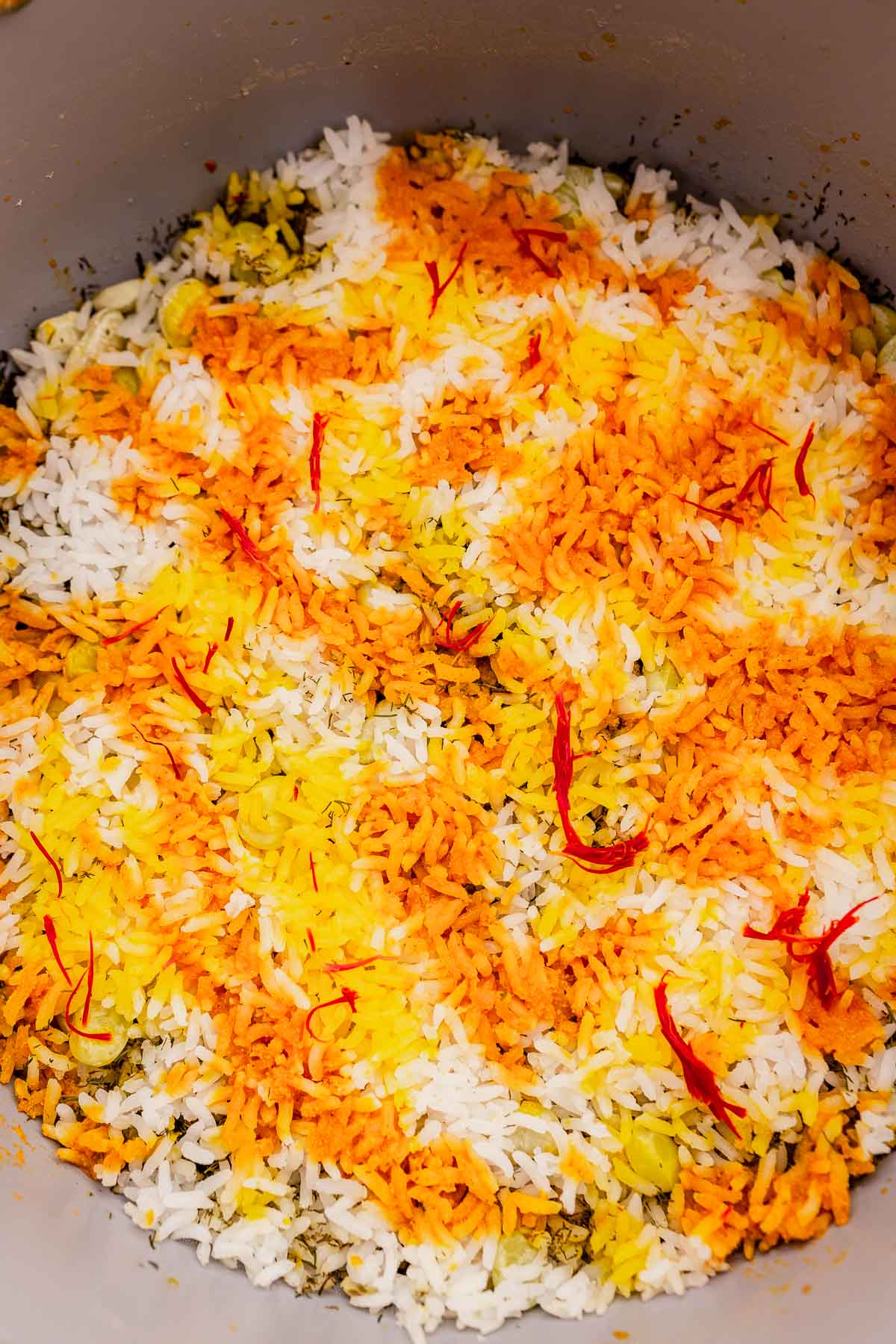 A close-up of vibrant dill rice adorned with saffron strands, showcasing a delightful mix of white, yellow, orange hues, and flecks of green.