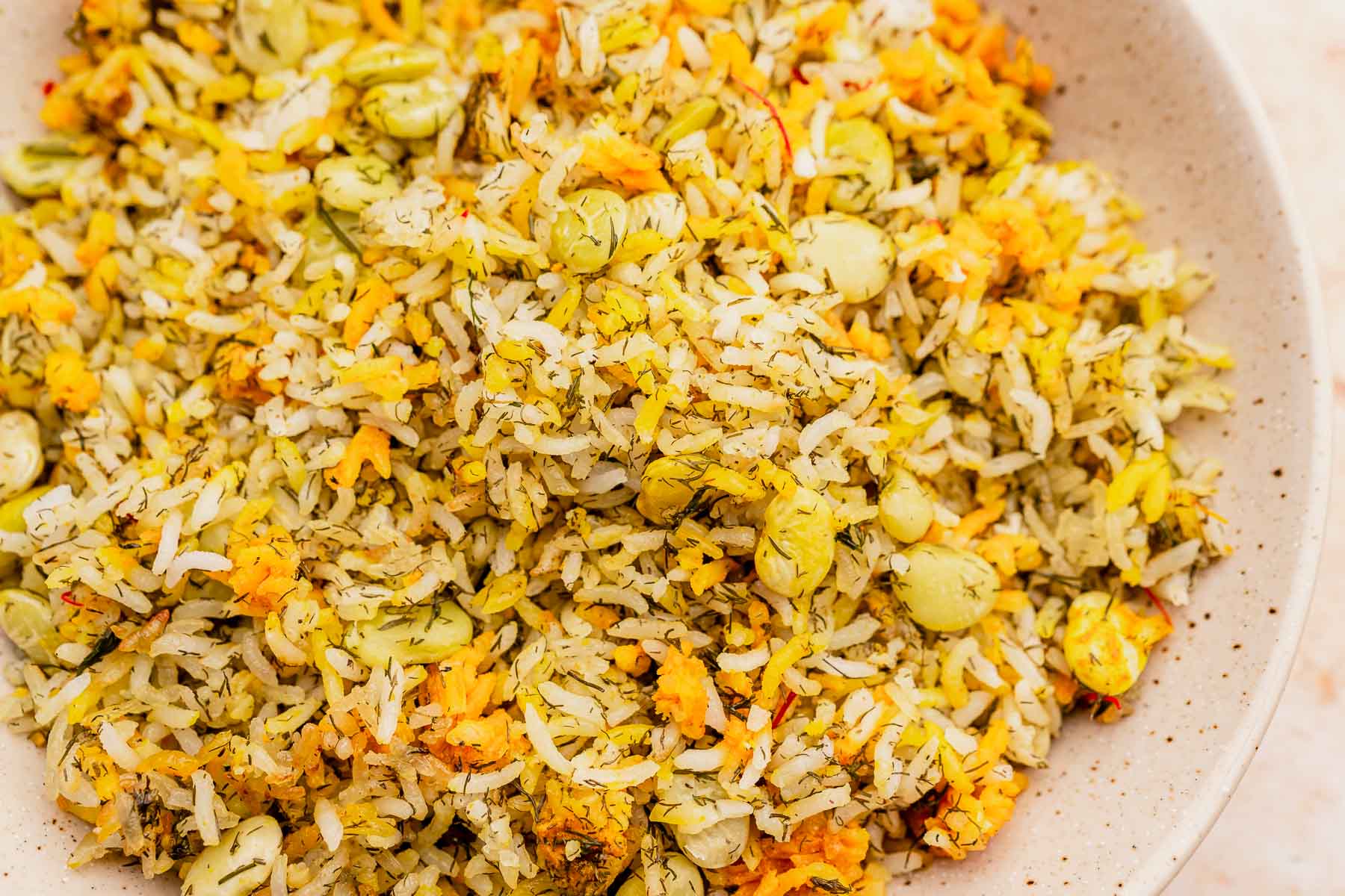 A close-up of a bowl featuring dill rice mixed with beans and grated orange vegetables, served on a speckled, beige plate.