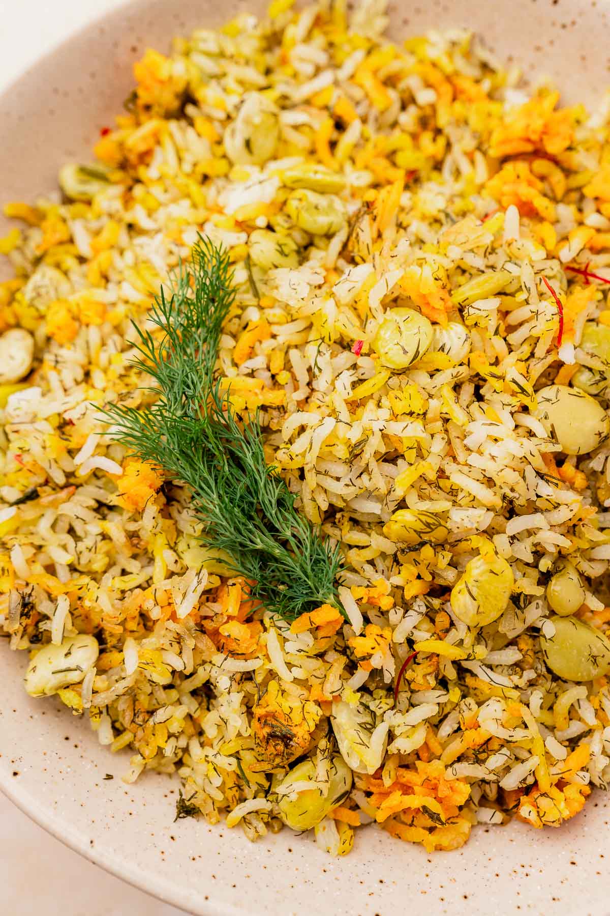 A bowl of dill rice infused with saffron and mixed with herbs and fava beans, garnished elegantly with a sprig of fresh dill.