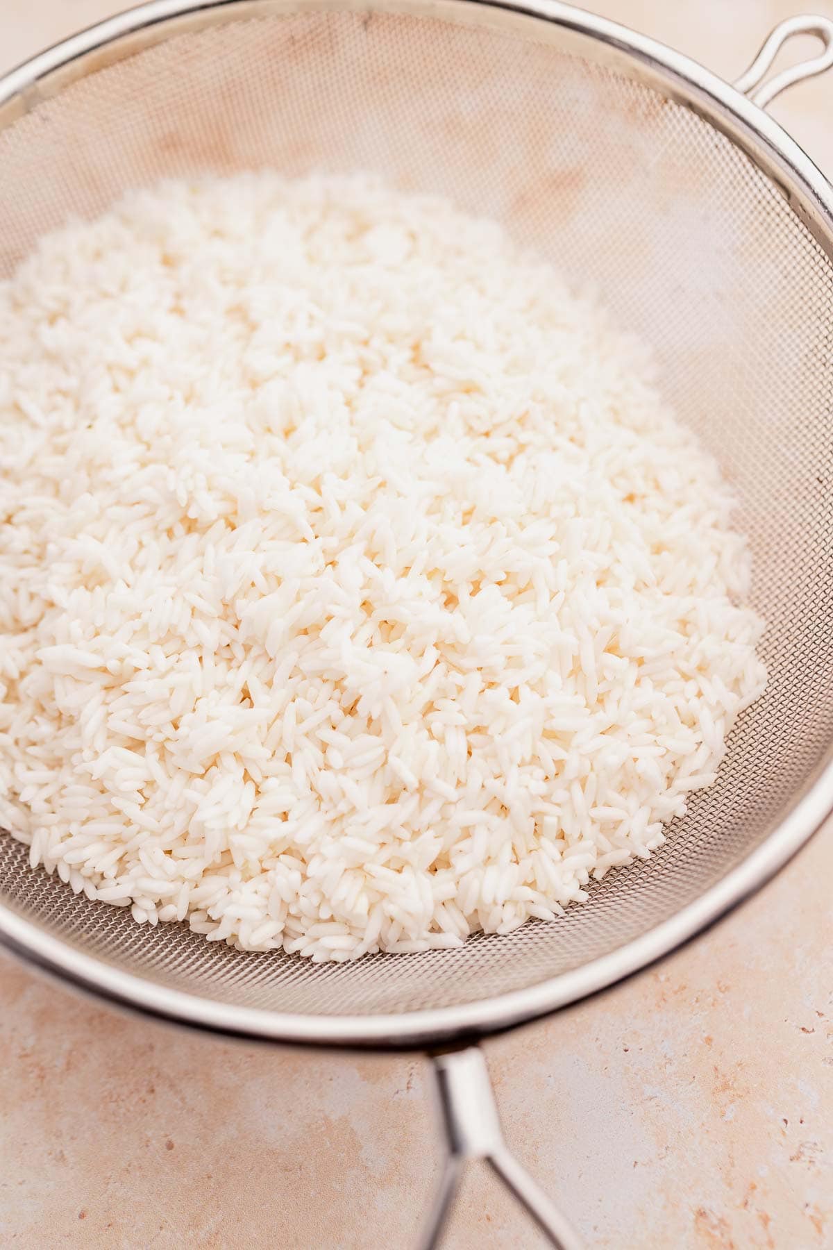 White rice in a metal sieve, ready to be transformed into fragrant dill rice, sits elegantly on a light-colored surface.