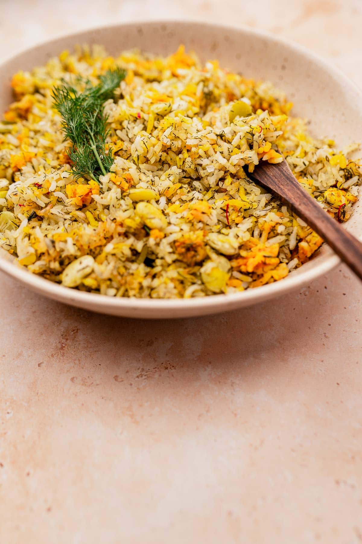 A vibrant bowl of dill rice mingled with fresh herbs and colorful vegetables, garnished with a sprig of dill, and accompanied by a wooden spoon resting on the side.