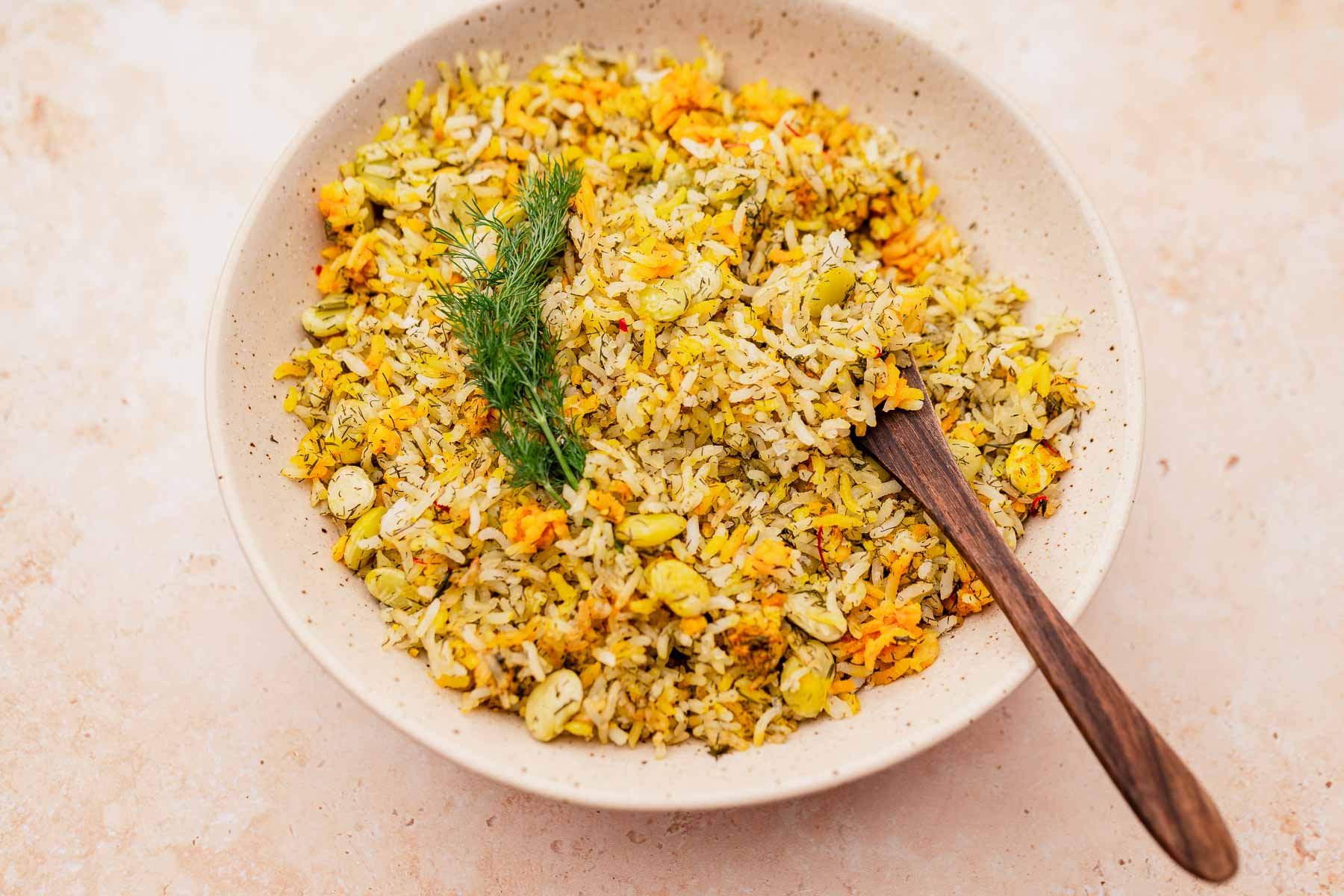 A bowl of dill rice mixed with fresh vegetables, garnished with sprigs of dill, and accompanied by a rustic wooden spoon.