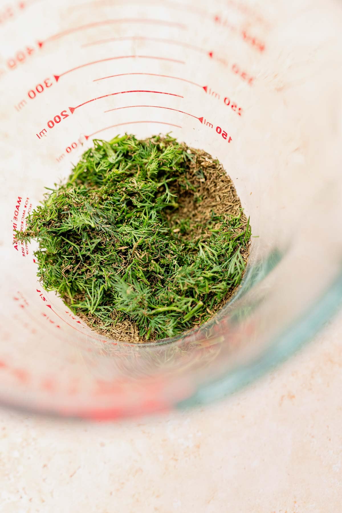 Freshly chopped green herbs are piled in a clear measuring cup on a light surface, ready to enhance your dill rice dishes with their vibrant aroma and flavor.