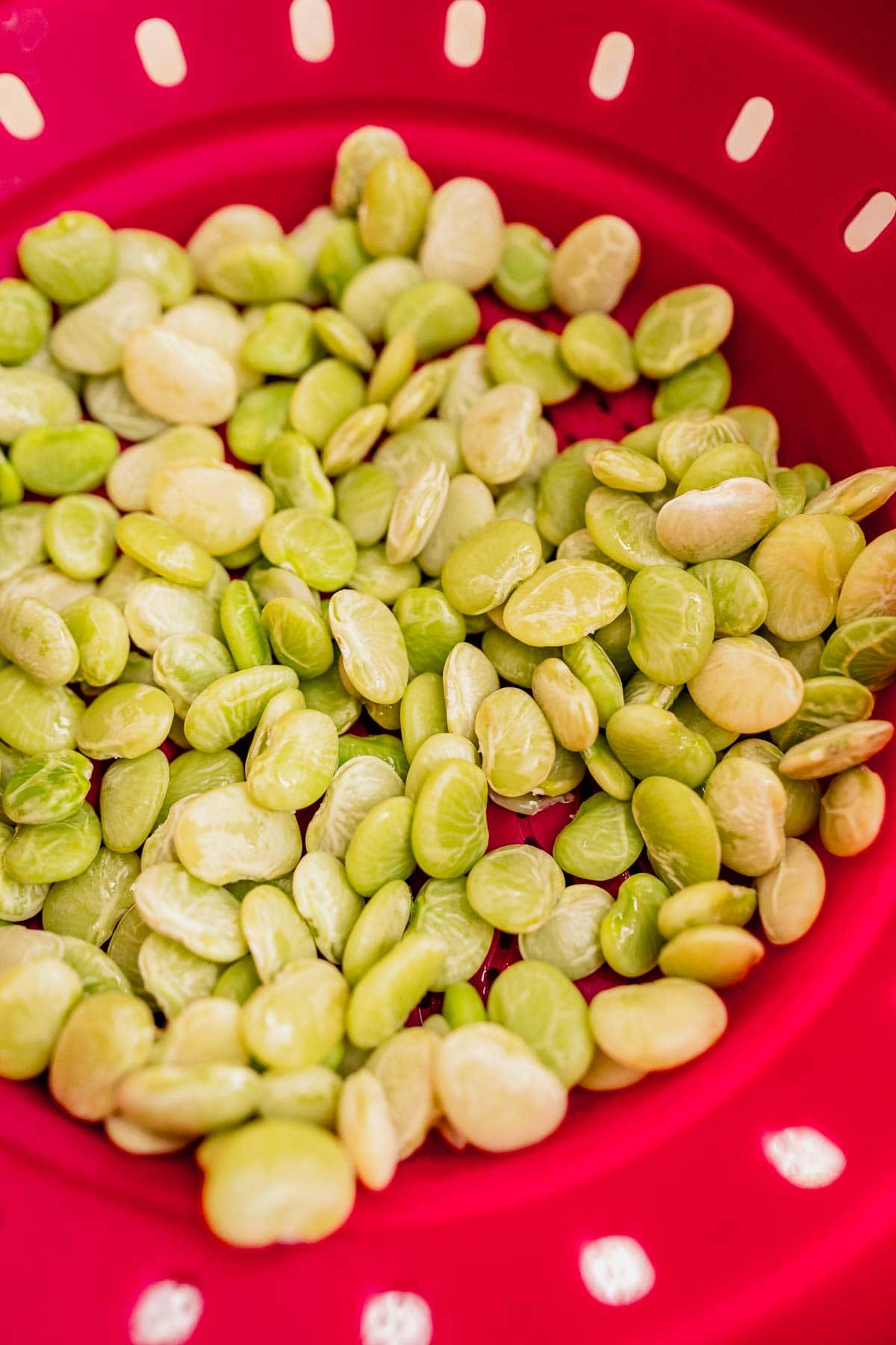 Close-up of a red colander holding a collection of light green lima beans, perfect for tossing into a dish with aromatic dill rice.