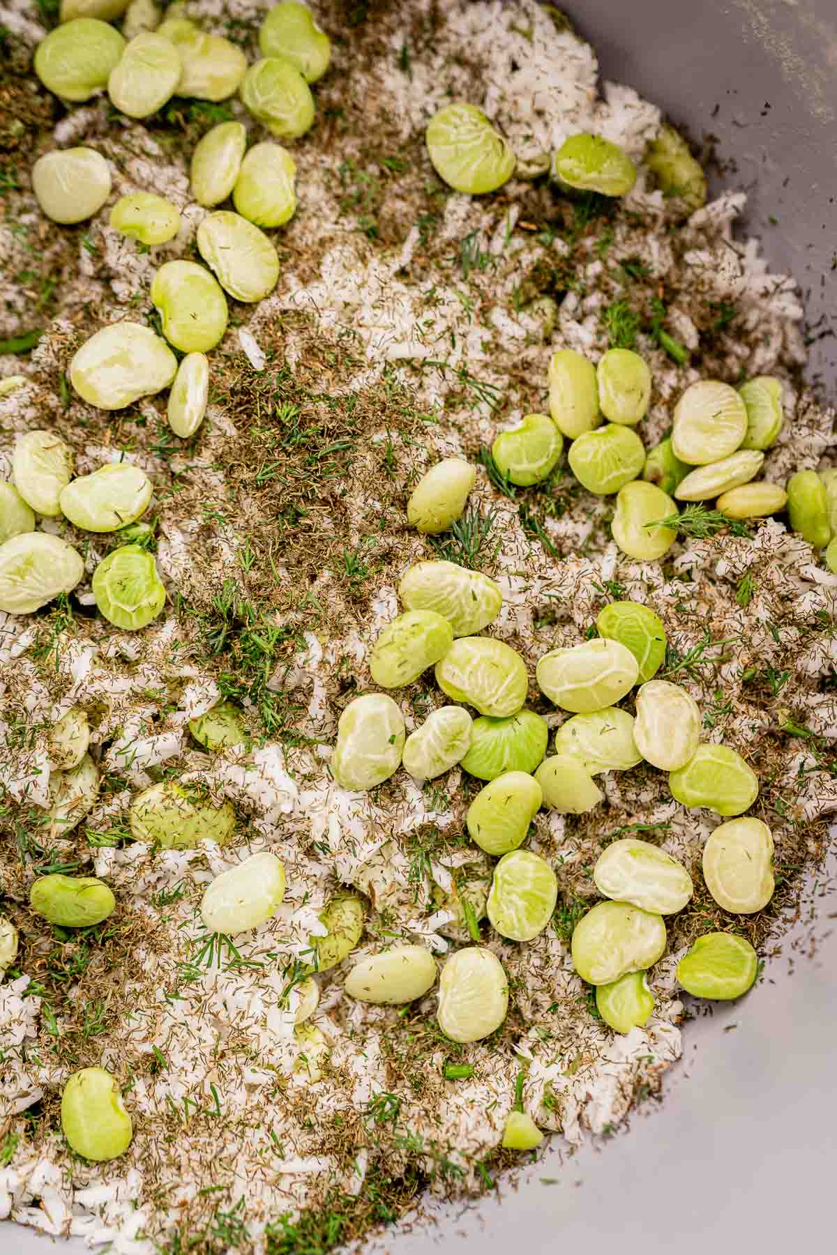 Close-up of uncooked dill rice mixed with green lima beans and sprinkled with herbs.