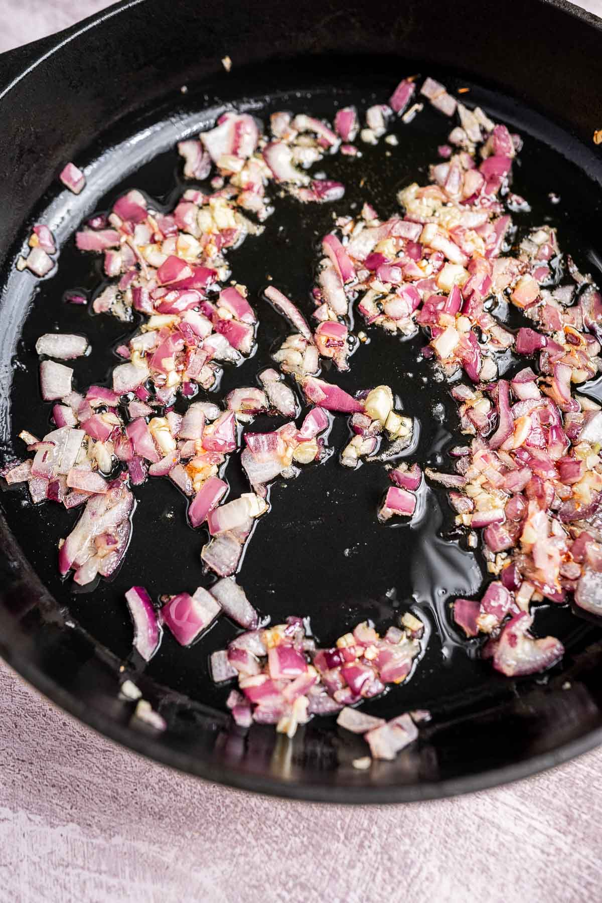 Chopped red onions and garlic sauté in a black skillet with oil, soon to be joined by fresh spinach and hearty chickpeas.