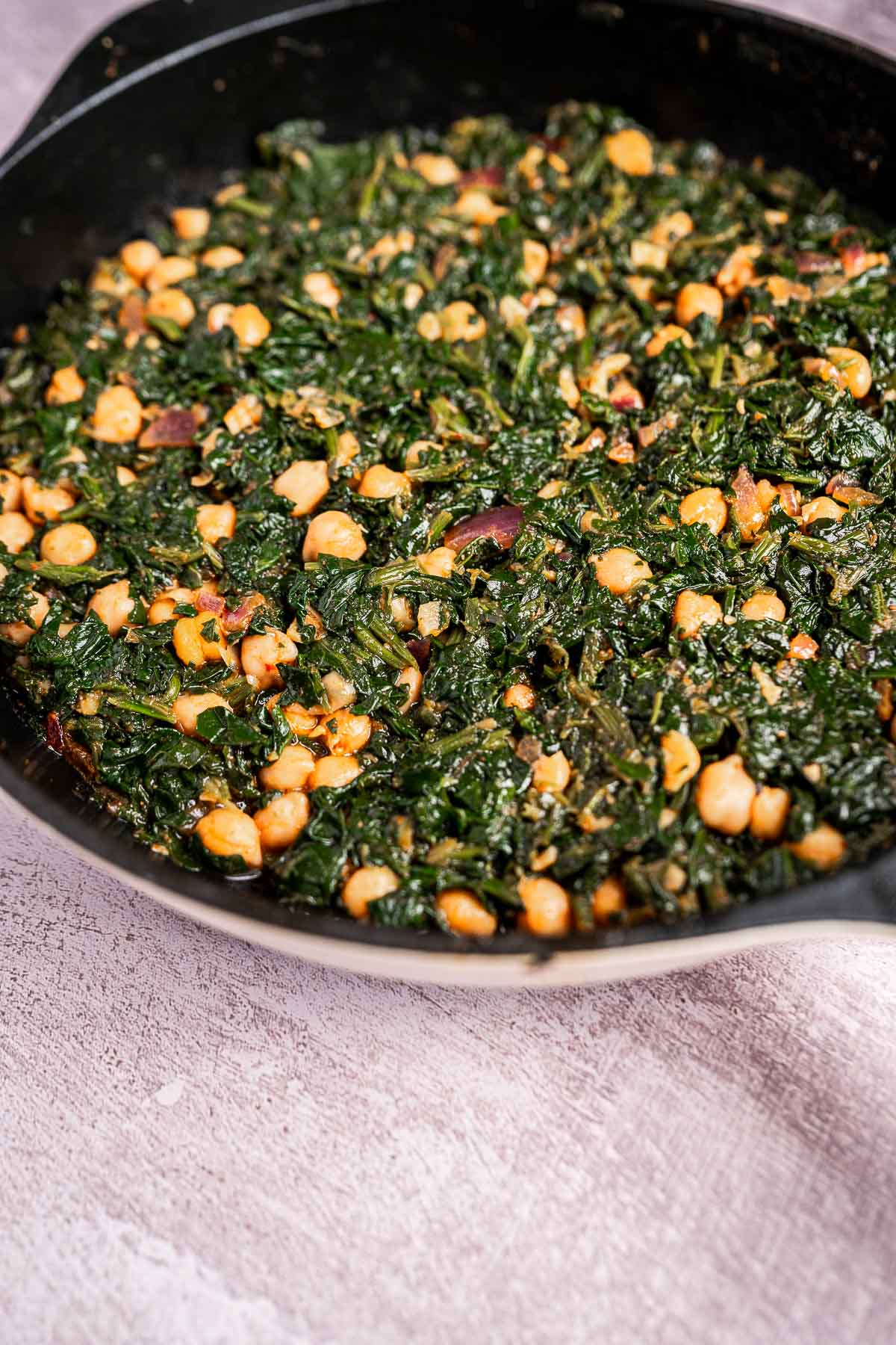 A skillet brimming with spinach and chickpeas rests on a textured surface, ready to delight your taste buds.