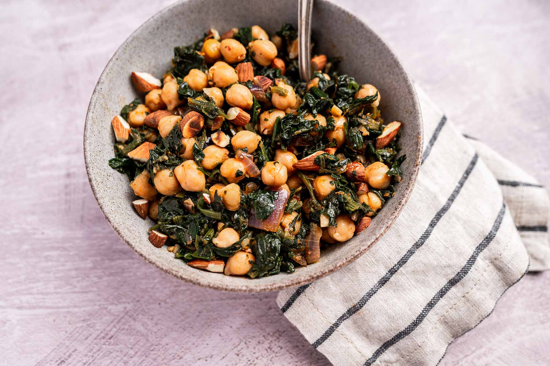 A vibrant bowl of spinach and chickpea salad with crunchy almonds, elegantly placed on a striped cloth.