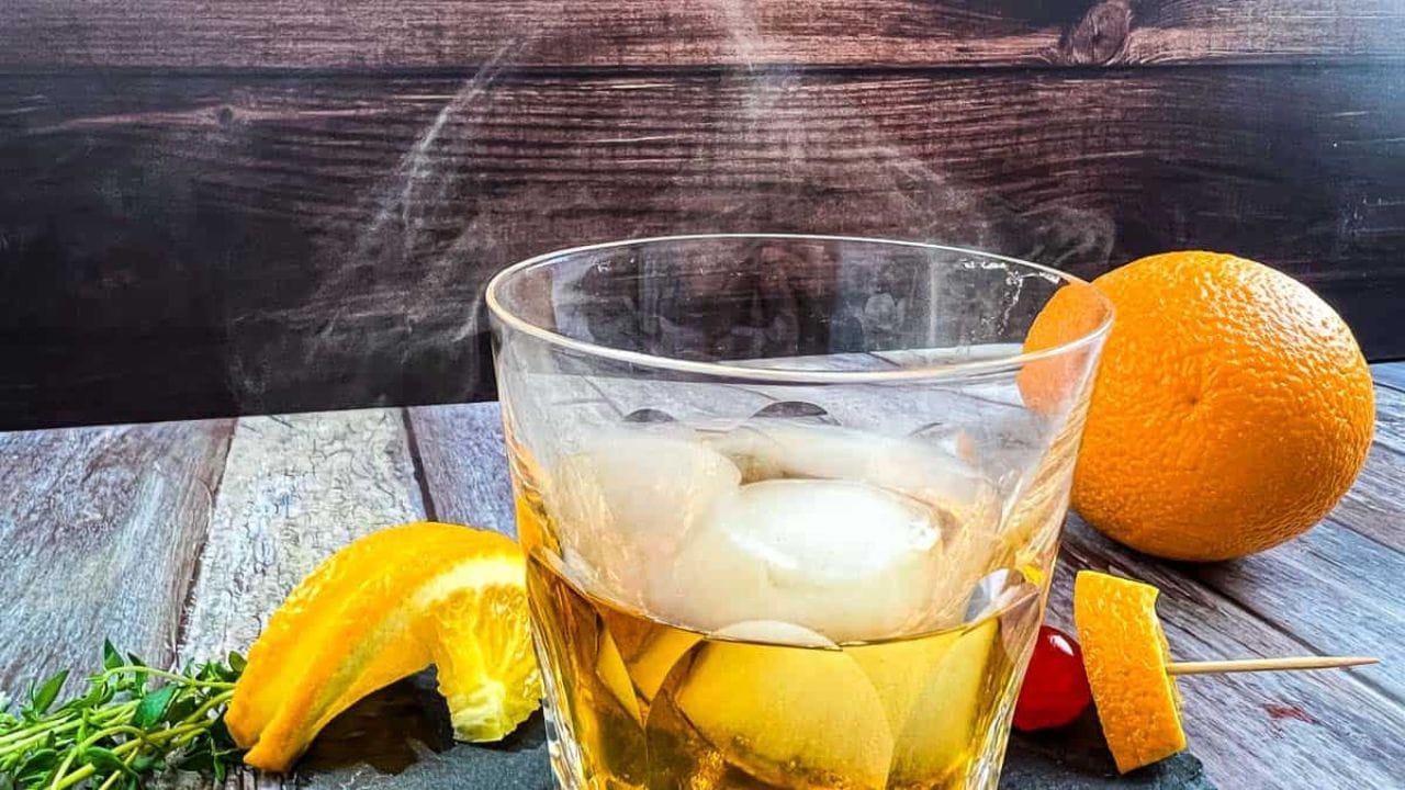 A glass of whiskey with oranges and a wooden stick.