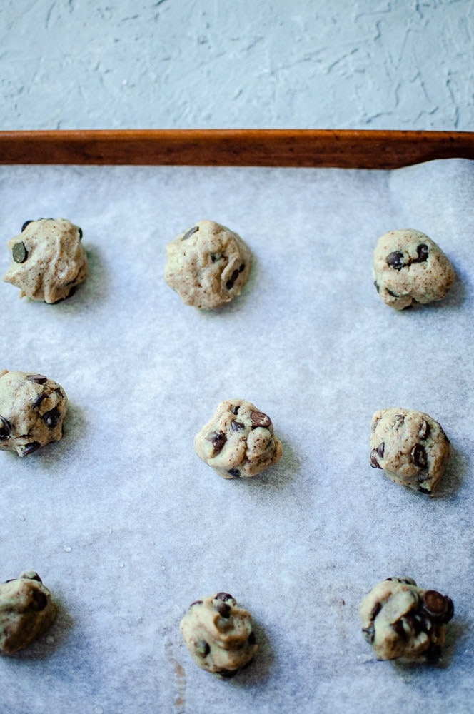 Sorghum flour cookies studded with chocolate chips are arranged on a parchment-lined baking sheet.